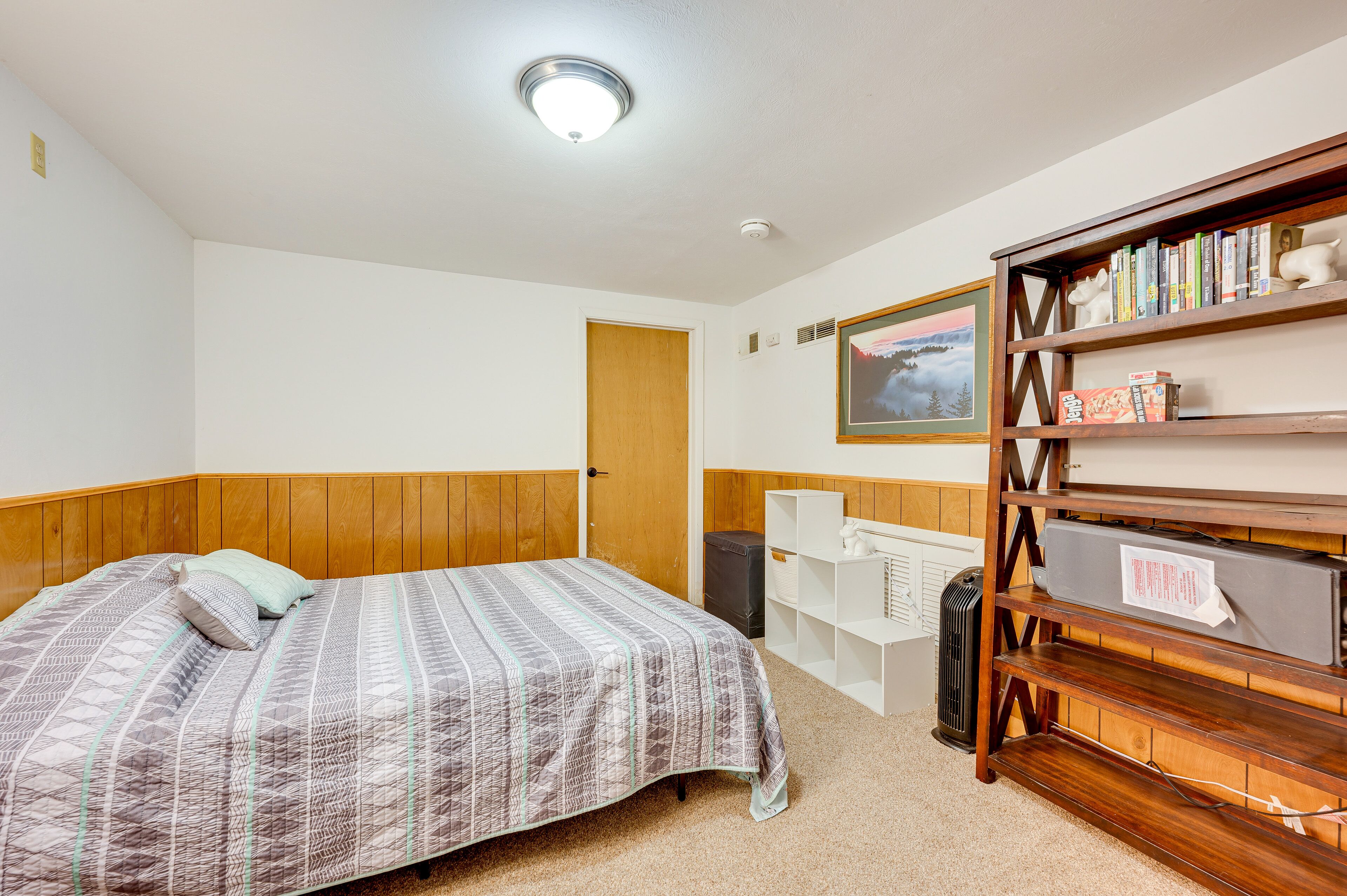 A bedroom with a bed, a bookshelf, a radiator, and a door.