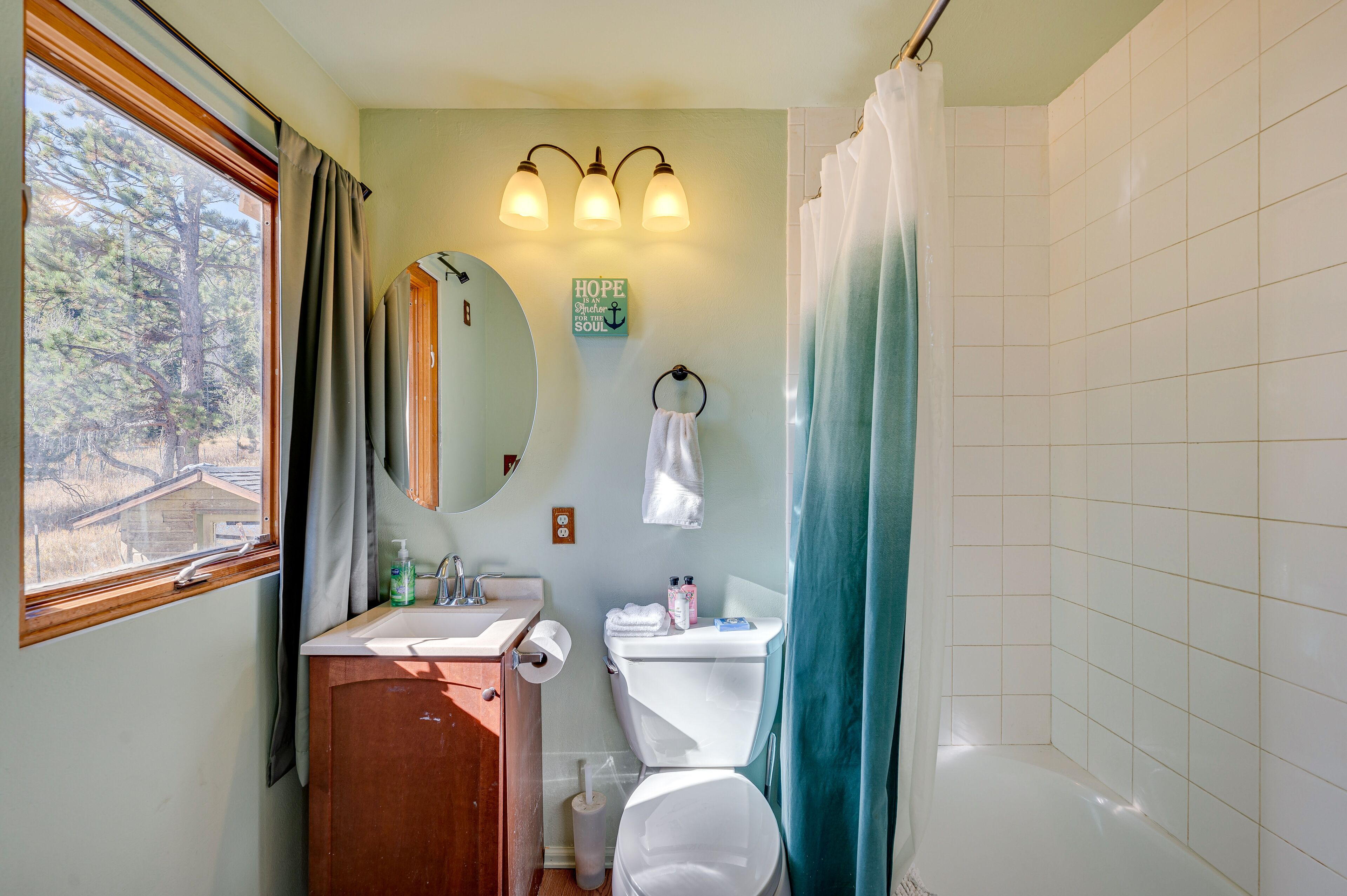 Un bagno con finestra, lavandino, specchio, WC e tenda della doccia.