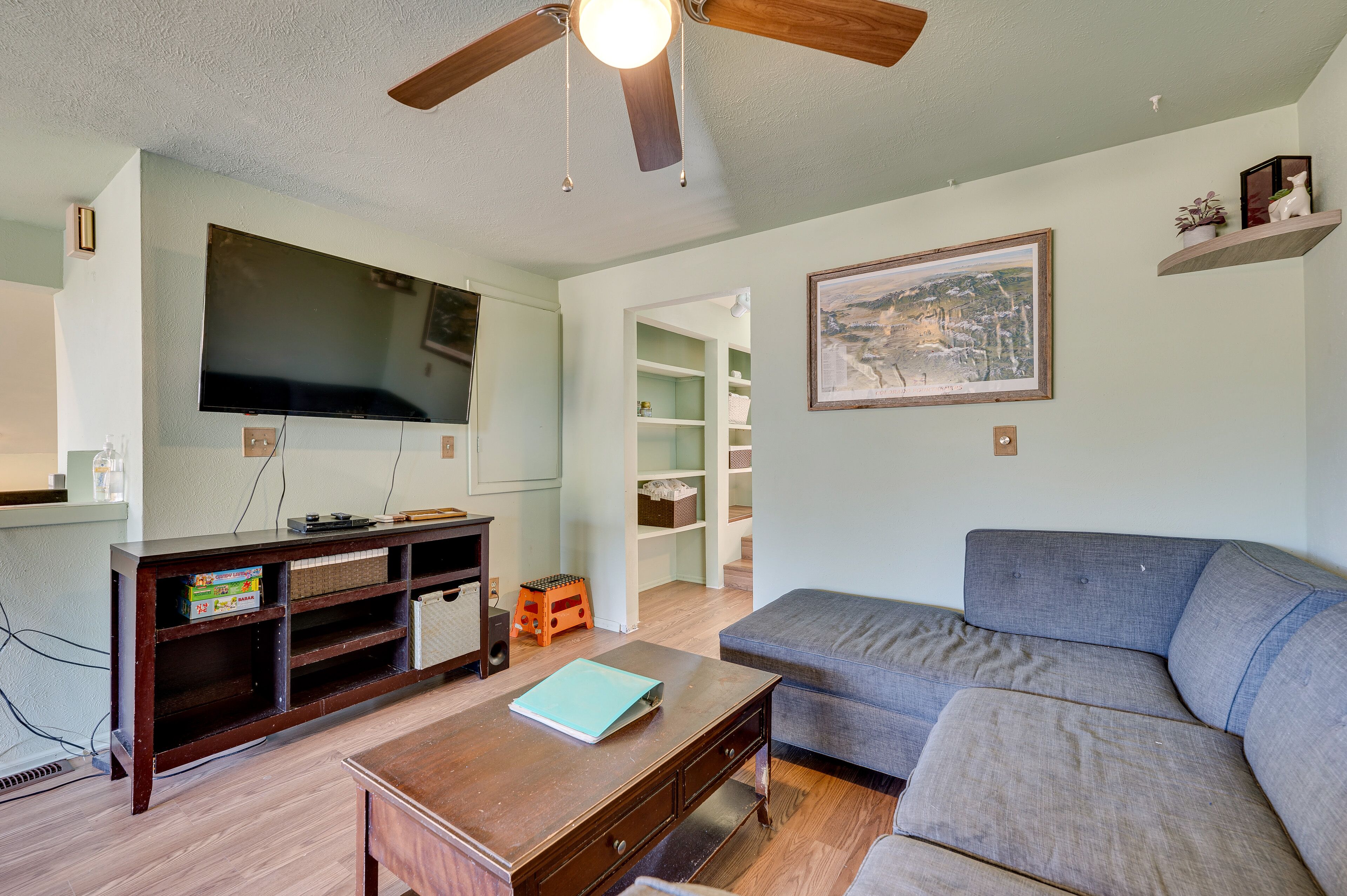Ein Wohnzimmer mit grauem Sofa, einer Holz-Unterhaltungseinrichtung, Fernseher und Deckenventilator.