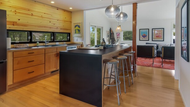 Una cocina moderna con armarios de madera, una isla central con taburetes, iluminación colgante y obras de arte en las paredes.