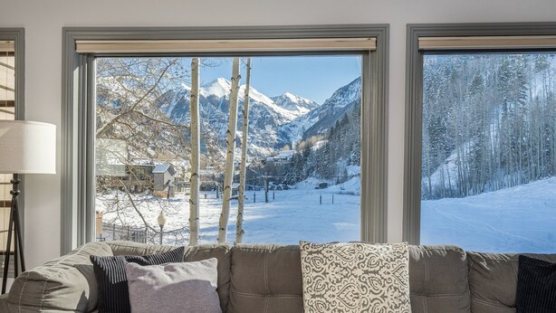 A living room with a sofa facing large windows offering a snowy mountain view.