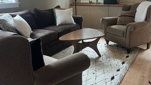 A cozy living room with a brown sofa, a brown armchair, a wooden coffee table, and a patterned rug. - Fly fishing, tubing, biking and shopping are steps away! (Sunderland)