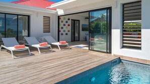 A modern outdoor pool area with lounge chairs and a wooden deck. - Modern villa ZYX with private pool, open-air cinema and 180° sea view (Saint-François)