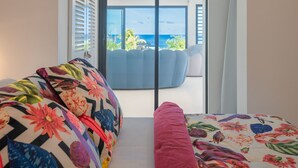 A room with a sofa and a bed, a sliding glass door leading to a balcony with a view of the ocean. - Modern villa ZYX with private pool, open-air cinema and 180° sea view (Saint-François)
