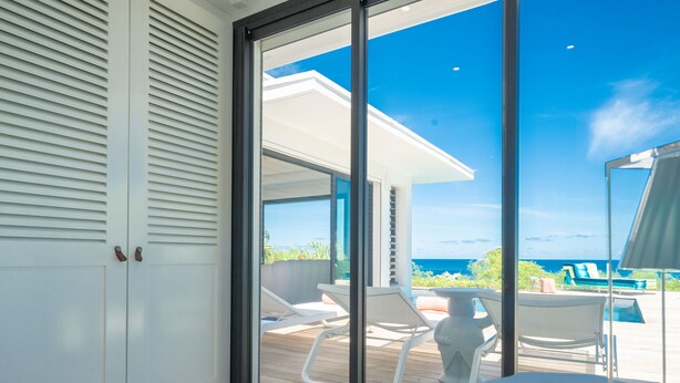 A modern room with a sliding glass door leading to an outdoor seating area with lounge chairs and a table. - Modern villa ZYX with private pool, open-air cinema and 180° sea view (Saint-François)