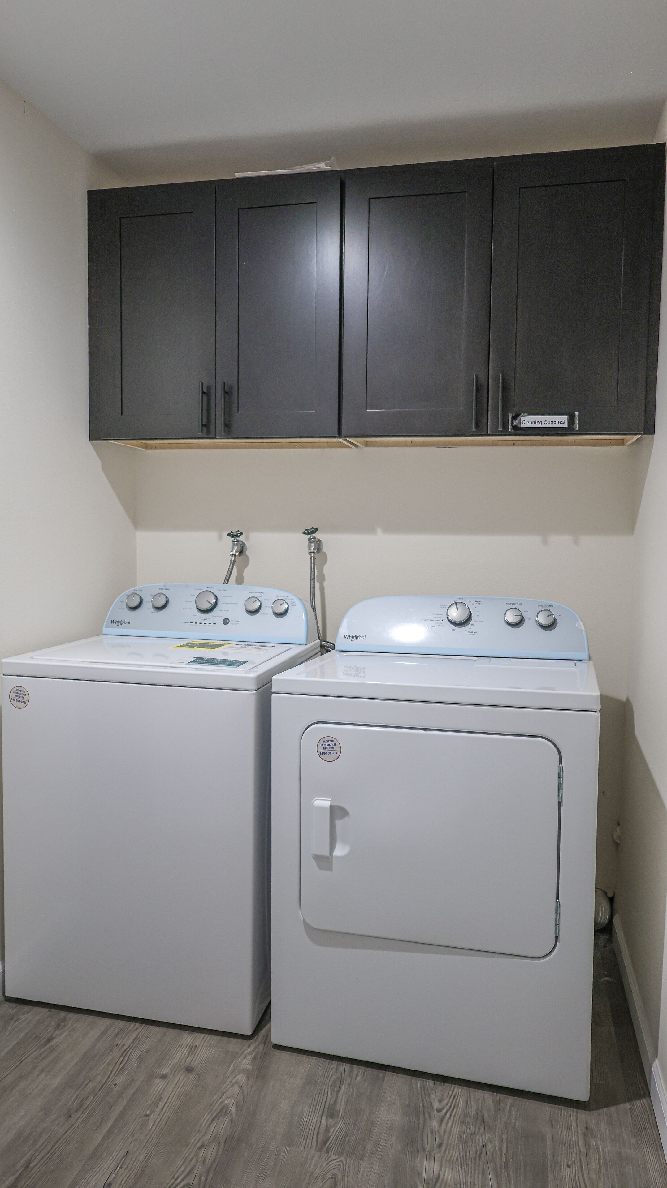 A laundry room with two white Whirlpool washers and a dark wooden cabinet above.