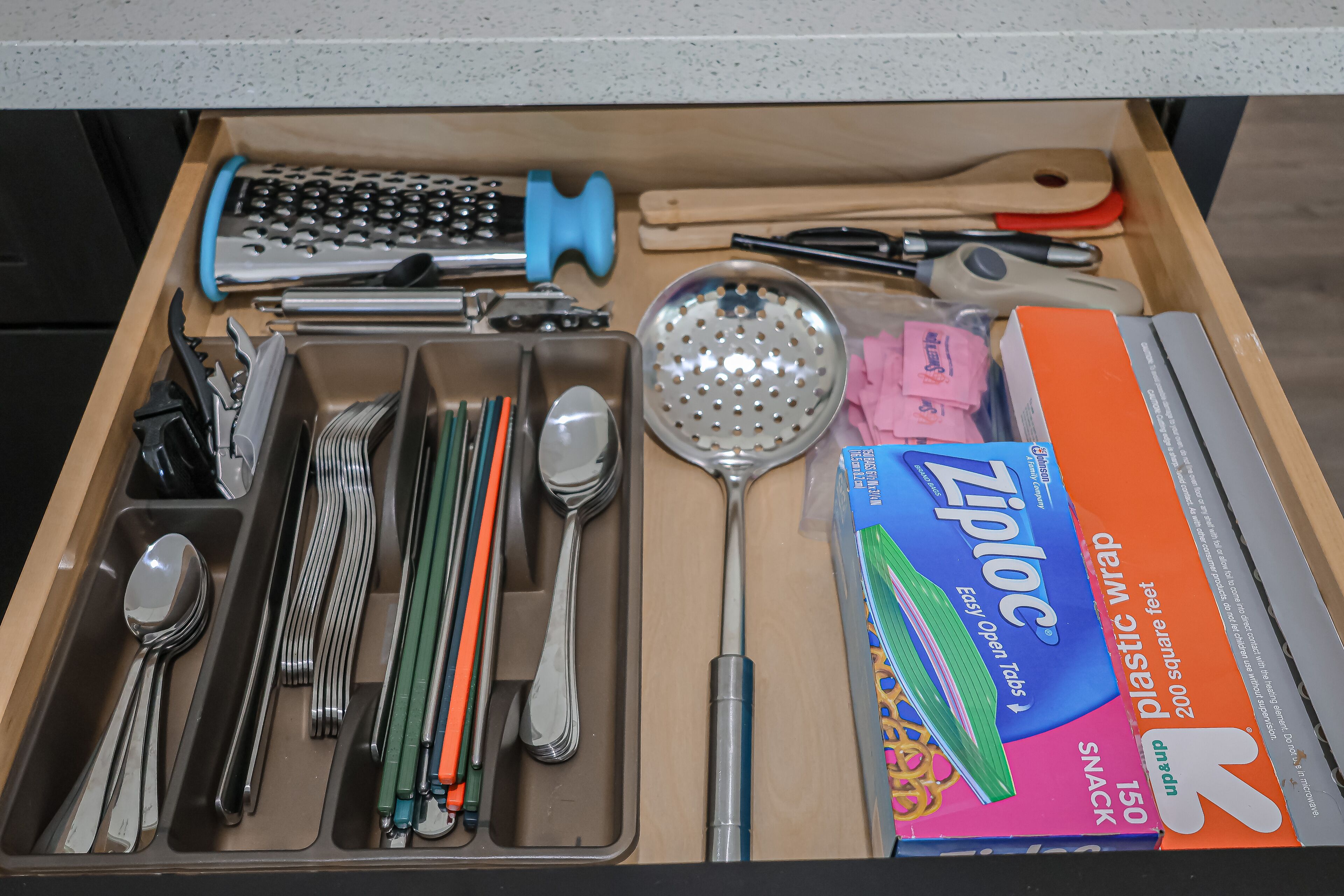 A drawer with various kitchen utensils including spoons, forks, knives, and a grater.