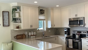A modern kitchen with white cabinets, a built-in island, stainless steel appliances, and a green cushioned bench. - The Spot on Sproat Lake (Port Alberni)