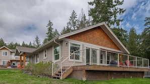 A two-story house with a wooden deck, a staircase leading to the deck, and a view of the surrounding forest. - The Spot on Sproat Lake (Port Alberni)