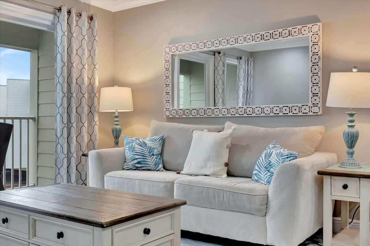 A room with a beige sofa, two side tables with lamps, a patterned curtain, and a decorative mirror on the wall.
