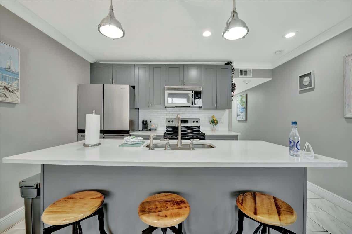 A modern kitchen with grey cabinets, a white countertop, and three wooden stools.
