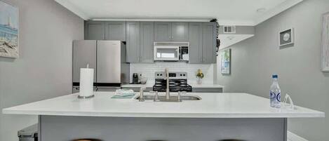 A modern kitchen with grey cabinets, a white countertop, and three wooden stools.