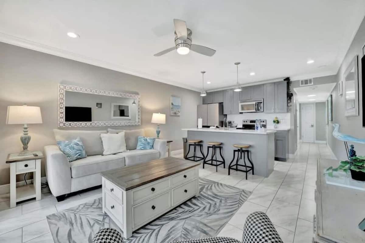 A modern living room with a sofa, coffee table, and a dining area with bar stools.