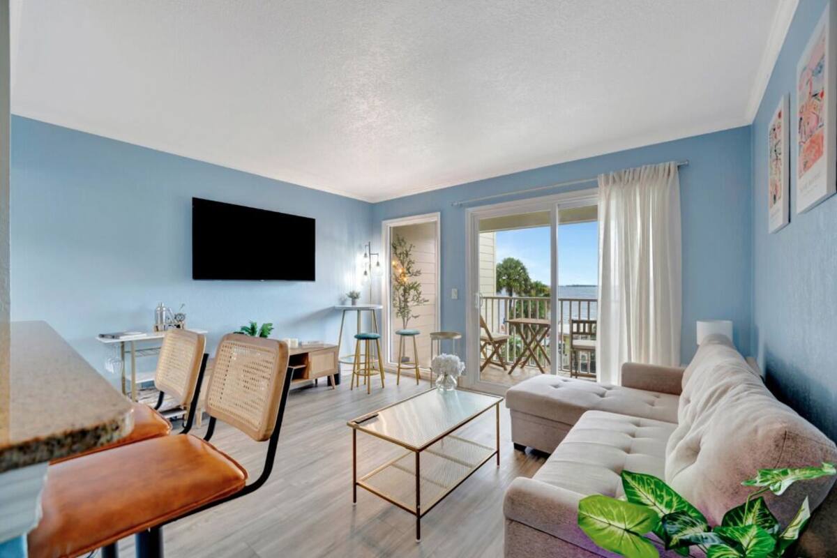 A living room with a sofa, coffee table, and chairs, a dining area with a table and chairs, and a balcony with a view.