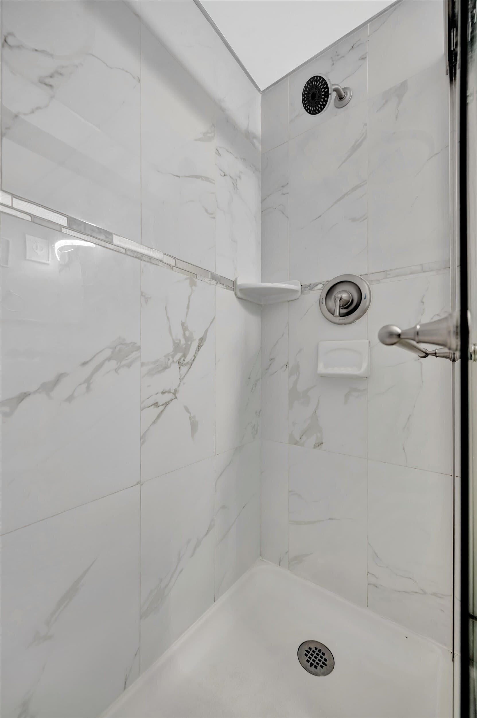 A modern shower with a marble wall, a handheld showerhead, and a built-in drain.