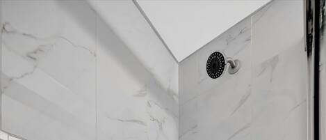A modern shower with a marble wall, a handheld showerhead, and a built-in drain.