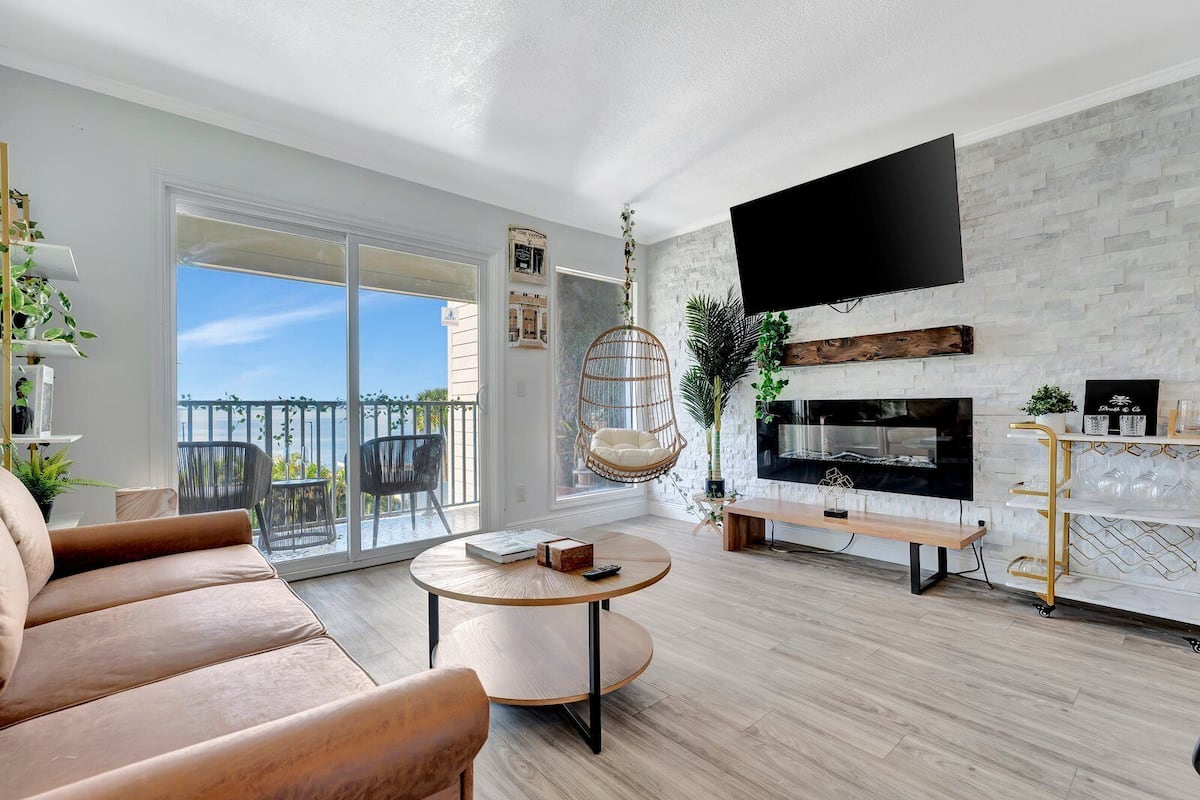 A modern living room with a sofa, a round coffee table, a hanging chair, a fireplace, and a TV mounted on a brick wall.