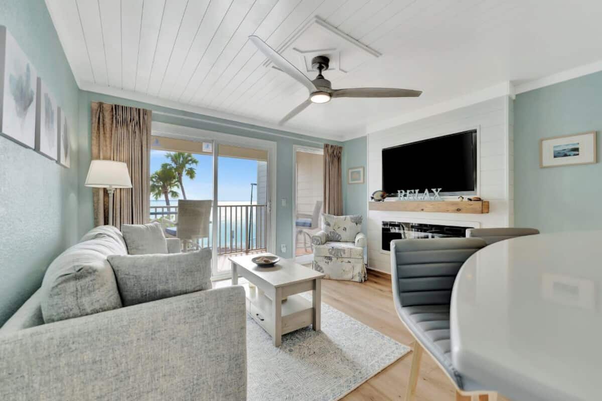 A living room with a sofa, armchair, TV, ceiling fan, and a view of the outdoors.
