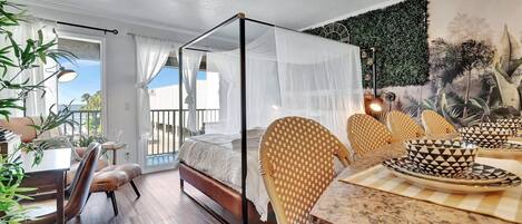 A bedroom with a four-poster bed, a dining area with patterned chairs and table, and a balcony with a view.