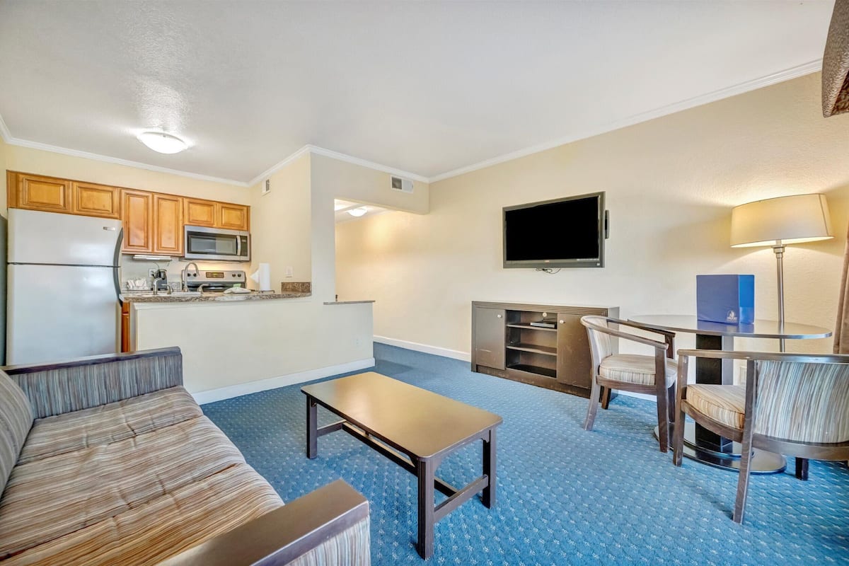 A compact living space with a kitchenette, a flat-screen TV, a sofa, a coffee table, and a dining area with chairs.