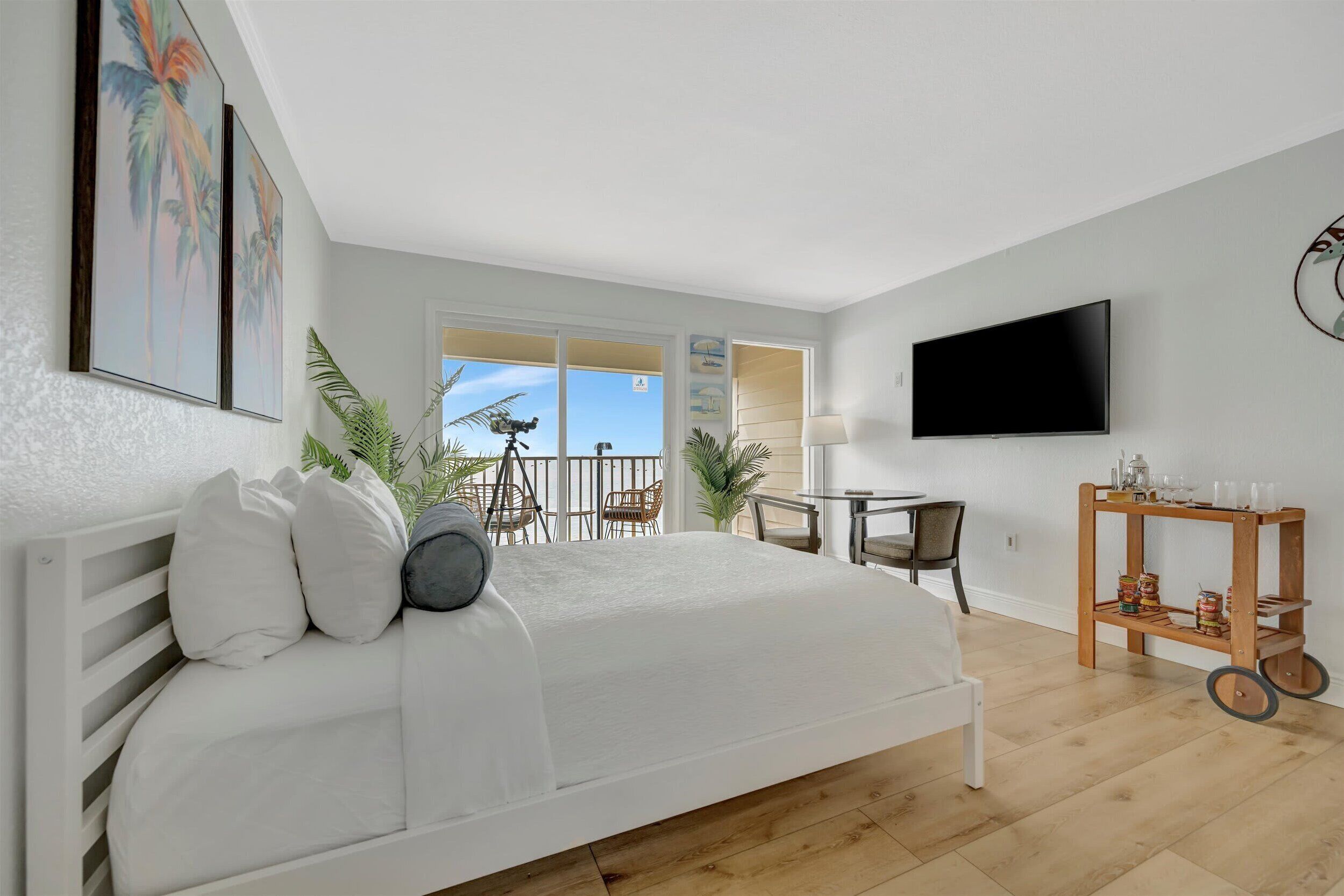 A modern bedroom with a large bed, a TV, and a balcony with outdoor furniture.
