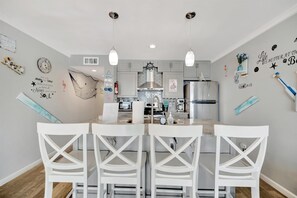 A modern kitchen with white cabinetry, pendant lights, and a central island with chairs. - The Hemingway (Tampa)
