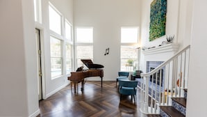 Un salón espacioso con un piano de cola, una escalera con escalones de diseño azul y blanco, y ventanas amplias que dejan entrar luz natural.