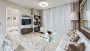 A modern living room with a sofa, a glass coffee table, a TV, and a white chair.