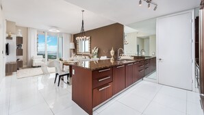 A modern kitchen with a large island, white cabinetry, and a view to the outside.