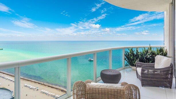 A balcony with wicker furniture, a view of the ocean, and a boat in the distance.