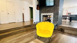 Una sala moderna con chimenea, un sillón amarillo brillante y una planta en maceta sobre una mesa de centro de madera.