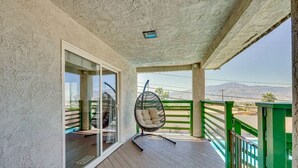 Un balcón con una hamaca colgante, vistas a las montañas y barandilla verde.