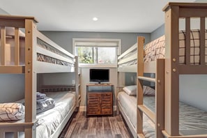 Quarto com beliches, televisão, mobiliário de madeira e janela.