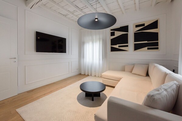 A modern living room with a sofa, a round coffee table, a flat-screen TV, and abstract wall art.