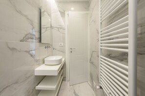 A bathroom with a white sink, marble walls, a door, and a towel rack.