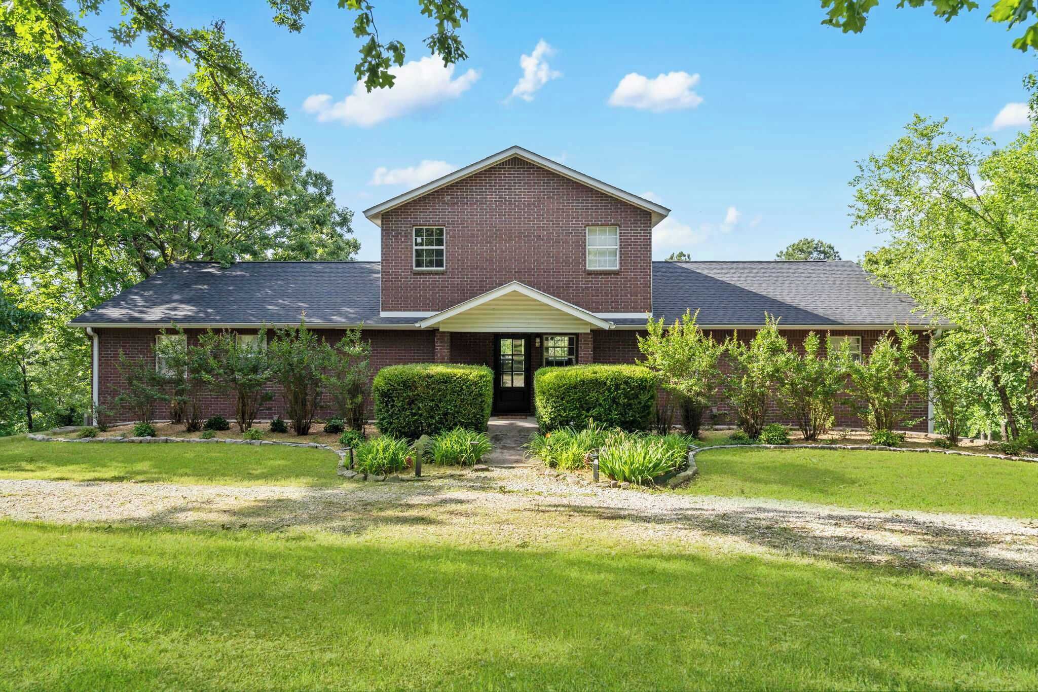 A two-story brick house with a front porch, surrounded by a well-maintained lawn and mature trees.