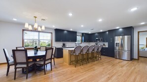 Una cucina moderna con pensili scuri, un frigorifero in acciaio inossidabile e un'area pranzo con sedie e tavolo in legno.