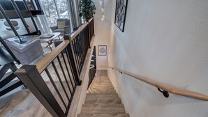 A wooden staircase with a black metal railing, leading to a room with a large window and a view of the outdoors. - Modern Paradise Getaway: Hot Tub, Mini Golf, Fire Pit, Dog Friendly, Parking (Colorado Springs)