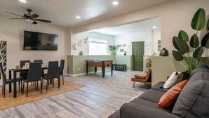 A living room with a gray sofa, a dining area with a table and chairs, a pool table, and a television mounted on the wall. - Tranquil Haven: Luxurious and Spacious Guest Suite
 (Colorado Springs)