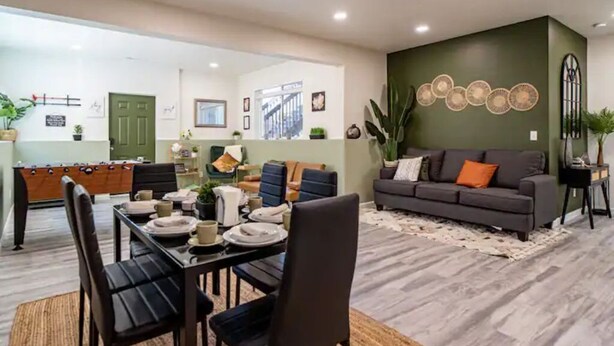 A modern living room with a dark green accent wall, a grey sofa with orange cushions, and a dining area with a table set for four. - Tranquil Haven: Luxurious and Spacious Guest Suite
 (Colorado Springs)