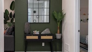 A hallway with a green wall, a mirrored wall, a wooden bench, and a potted plant. - Tranquil Haven: Luxurious and Spacious Guest Suite
 (Colorado Springs)
