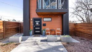 En moderne bygning med en sort dør, en balkon med udendørs siddepladser og et skilt med adresseangivelse.