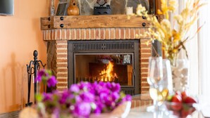 A fireplace with a fire, a wooden mantel, and a vase with flowers.