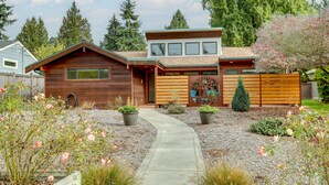 A modern house with a wooden exterior, a covered porch, and a landscaped garden with roses and shrubs. - Near Eats & Brews! Beautiful Seattle Home w/ Patio (Seattle)