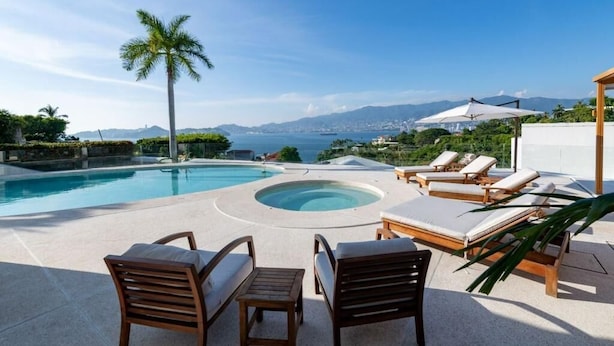 Ein Poolbereich mit Liegestühlen und einem Whirlpool, mit Blick auf eine malerische Aussicht auf das Meer und die Berge.