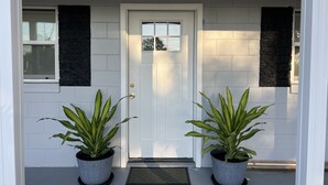A front door with two potted plants on either side, a window, and a doorbell mat.