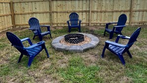 A backyard with a wooden fence, a fire pit, and four Adirondack chairs arranged in a circle.