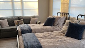 A bedroom with two beds, a sofa, and large windows.