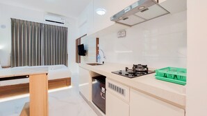 Una cocina moderna con estufa integrada, pileta y lavavajillas. Hay una mesa de madera y una cama en la habitación contigua.