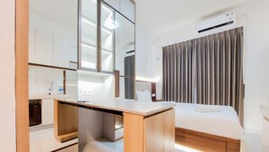 Una habitación pequeña con escritorio de madera, cama, espejo y aire acondicionado.